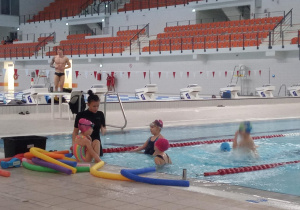 Dzieci w basenie słuchają instrukcji trenerki.