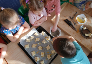 Dzieci siedzą wokół stołu i ozdabiają przygotowane ciasteczka.