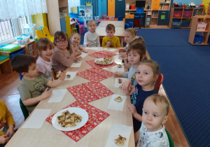 Dzieci siedzą przy stołach i zjadają przygotowane przez siebie ciasteczka.