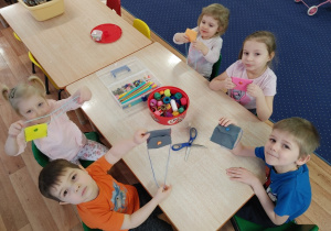 Dzieci siedzą przy stole i prezentują swoje własnoręcznie uszyte portfele.