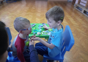 Chłopcy siedzą naprzeciwko siebie. Jeden z nich bada stetoskopem drugiego.