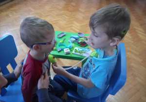 Chłopcy siedzą naprzeciwko siebie. Jeden z nich bada stetoskopem drugiego.