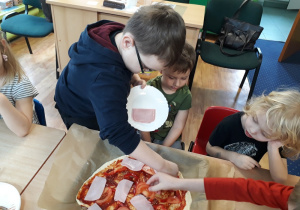 dzieci samodzielnie dekorują pizzę