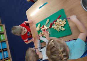 troje dzieci kroją owoce na plastikowych tacach