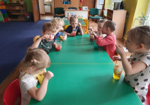 dzieci siedzą przy stolikach i jedzą galaretkę