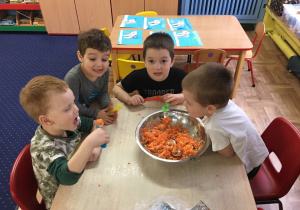 dzieci siedzą przy stoliku i próbują surówkę z warzyw