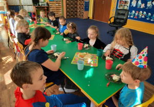 Dzieci siedzą przy stole i zjadają tort.