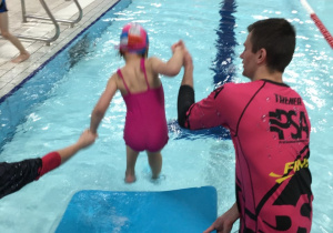 Dziewczynka wchodzi do wody przy asekuracji instruktorów.