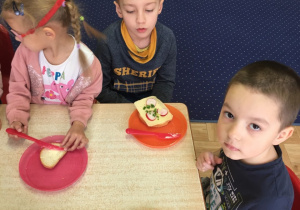 Dzieci siedzą przy stole, a na talerzach leżą samodzielnie przygotowane kanapki.