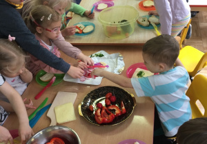 Dzieci siedzą przy stole i przygotowują kanapki dla siebie.
