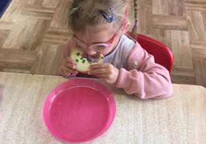 Dziewczynka siedzi przy stole i zjada swoją kanapkę.