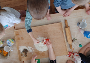 Dzieci zgromadzone wokół stołu przygotowują ciasto na faworki.
