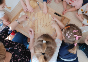 Dzieci zgromadzone wokół stołu na którym znajduje się stolnica z pociętym ciastem na faworki.