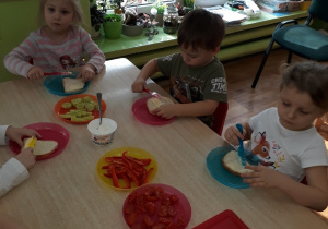 Dzieci siedzą przy stole i przygotowują kanapki.