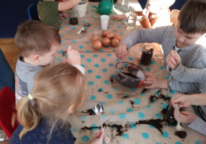 Dzieci siedzą przy stole i wsypują ziemię do słoików.