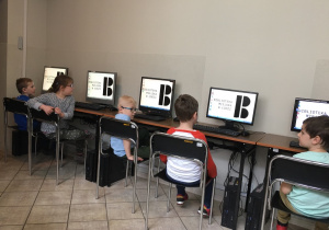 Dzieci siedzą na krzesłach przed komputerami.