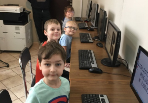 Dzieci siedzą na krzesłach przed komputerami.