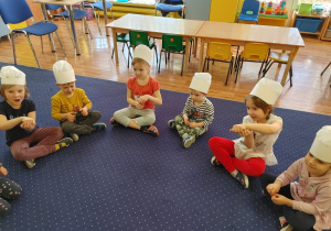 dzieci razem z panią siedzą w kole, na głowach mają czapki kucharskie