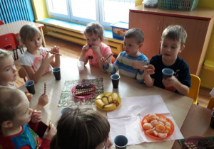 Dzieci przy stole jedzą słodycze.