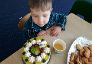Chłopiec siedzi przy stole na którym stoi tort.