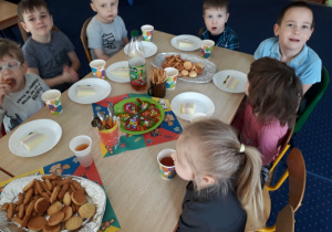 Dzieci siedzą przy stole na którym są słodkości.