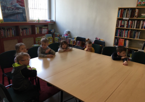 Dzieci siedzą przy stole w bibliotece.