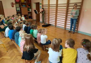 Dzieci siedzą na sali gimnastycznej i słuchają koncertu. Absolwentka gra na skrzypcach.