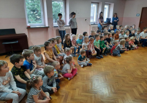 Dzieci siedzą na sali gimnastycznej i słuchają koncertu.