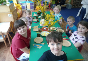 dzieci siedzą przy stolikach z wielkanocnymi potrawami