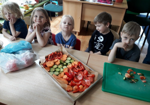 dzieci siedzą przy stoliku, na którym widać pokrojone warzywa