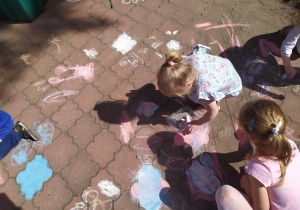 Dzieci rysują kredą po chodniku.
