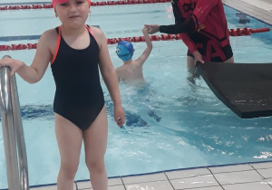 Dziewczynka wychodzi z wody, chłopiec ćwiczy swoje umiejętności pływackie w wodzie.