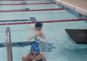 Chłopiec wychodzi z wody, drugi ćwiczy swoje umiejętności pływackie w wodzie.