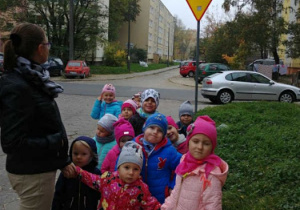 Dzieci przy ulicy pokazują znak drogowy.