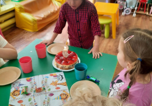 Dzieci siedzą przy stole, a chłopiec zdmuchuje świeczkę.