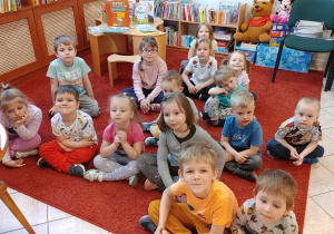 dzieci siedzą na czerwonym dywanie w bibliotece