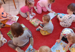 dzieci siedzą na czerwonym dywanie w bibliotece, oglądają książki