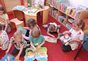 dzieci siedzą na czerwonym dywanie w bibliotece, oglądają książki