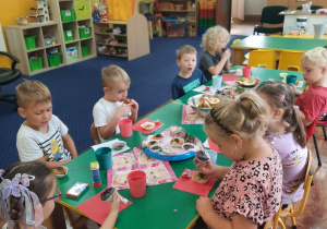 Dzieci siedzą przy stole i zjadają słodkości.