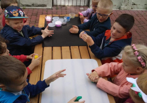dzieci siedzą przy stole na tarasie i lepią z plastopianki