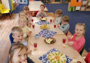Dzieci siedzą przy stole i zjadają poczęstunek przygotowany przez panie..