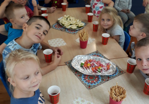 Dzieci siedzą przy stole na którym znajdują się smakołyki.