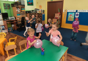 Dwie dziewczynki przy stole ozdabiają balony, pozostałe dzieci bawią się balonami już ozdobionymi.