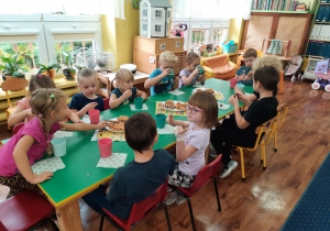 Dzieci siedzą przy stole i zjadają smakołyki .