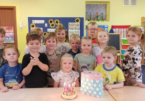 dziewczynka zdmuchuje świeczki z urodzinowego tortu, dzieci stoją wokół niej