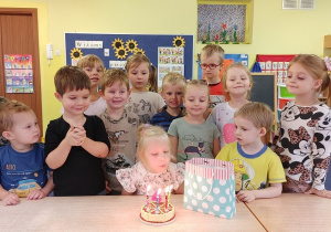 dziewczynka zdmuchuje świeczki z urodzinowego tortu, dzieci stoją wokół niej