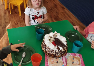 Dziewczynka siedzi przy stole na którym stoi tort.