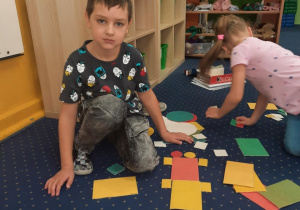 Chłopiec siedzi obok swojej kompozycji z figur geometrycznych.