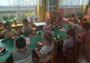 Dzieci siedzą przy stole i zjadają smakołyki.