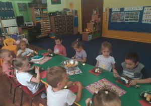 Dzieci siedzą przy stole i zjadają smakołyki.